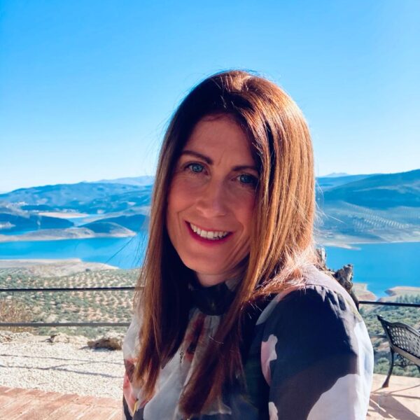 The coach appears smiling with lake scenery in the background.