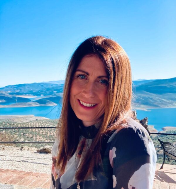 The coach appears smiling with lake scenery in the background.